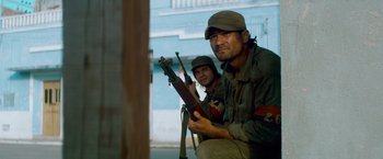 Movie still from “Che: Part One” (2008), directed by Steven Soderbergh – A man and a woman holding guns while sitting on the ground; Medium shot, Low angle