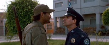 Movie still from “Che: Part One” (2008), directed by Steven Soderbergh – Two police officers talking to each other outside a building; Close Up shot, Over the shoulder angle