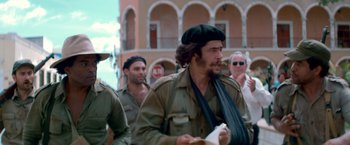 Movie still from “Che: Part One” (2008), directed by Steven Soderbergh – A group of men in military uniforms walking down a street; Medium shot, Low angle