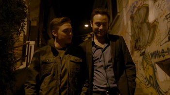 Movie still from “Chernobyl Diaries” (2012), directed by Bradley Parker – A couple of men standing next to each other on a street; Medium shot, Over the shoulder angle