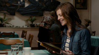 Movie still from “Chernobyl Diaries” (2012), directed by Bradley Parker – A woman sitting at a table looking at an open book; Medium shot, Over the shoulder angle