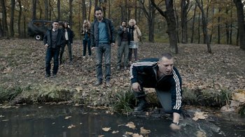 Movie still from “Chernobyl Diaries” (2012), directed by Bradley Parker – A man crouching in the grass near a body of water; Wide shot, High angle