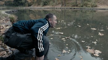 Movie still from “Chernobyl Diaries” (2012), directed by Bradley Parker – A man crouching in the water near a body of water; Medium shot, High angle