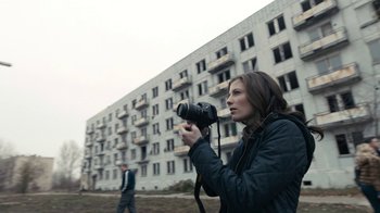 Movie still from “Chernobyl Diaries” (2012), directed by Bradley Parker – A woman holding a camera in front of an apartment building; Medium shot, Low angle