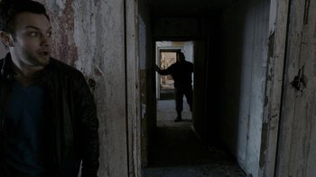 Movie still from “Chernobyl Diaries” (2012), directed by Bradley Parker – A man in a black jacket is walking through an open door; Medium shot, Over the shoulder angle