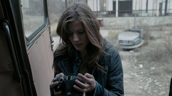 Movie still from “Chernobyl Diaries” (2012), directed by Bradley Parker – A woman holding a camera while standing in front of a building; Close Up shot, High angle