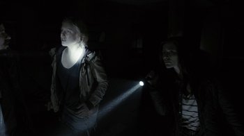 Movie still from “Chernobyl Diaries” (2012), directed by Bradley Parker – Two women are standing in the dark with a flashlight in their hand; Medium shot, Over the shoulder angle