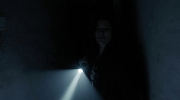 Movie still from “Chernobyl Diaries” (2012), directed by Bradley Parker – A woman is holding a flashlight in the dark; Medium shot, Low angle