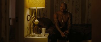 Movie still from “Chi-Raq” (2015), directed by Spike Lee – A man sitting on a chair next to a table with a lamp; Medium shot, Over the shoulder angle