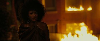 Movie still from “Chi-Raq” (2015), directed by Spike Lee – A black woman with a big curly afro is standing in front of a building; Close Up shot, Over the shoulder angle