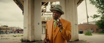Movie still from “Chi-Raq” (2015), directed by Spike Lee – An older man in an orange suit and a green hat; Medium shot, Over the shoulder angle