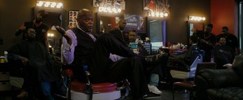 Movie still from “Chi-Raq” (2015), directed by Spike Lee – A man sitting in a chair in front of two other men; Medium shot, Over the shoulder angle