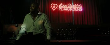 Movie still from “Chi-Raq” (2015), directed by Spike Lee – A man standing in front of a bar in front of a neon sign; Medium shot, Over the shoulder angle