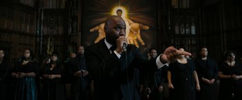 Movie still from “Chi-Raq” (2015), directed by Spike Lee – A man in a black suit is singing into a microphone; Medium shot, Low angle