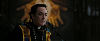 Movie still from “Chi-Raq” (2015), directed by Spike Lee – A man in a priest's outfit is speaking at a microphone; Close Up shot, Low angle