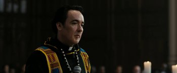 Movie still from “Chi-Raq” (2015), directed by Spike Lee – A man in a priest's outfit with a microphone in front of him; Close Up shot, Low angle