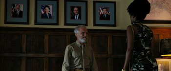 Movie still from “Chi-Raq” (2015), directed by Spike Lee – An older man standing in front of a wall with three pictures on the wall behind him; Medium shot, Low angle