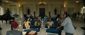 Movie still from “Chi-Raq” (2015), directed by Spike Lee – A group of people sitting on blue couches in a room; Extreme Wide shot, High angle