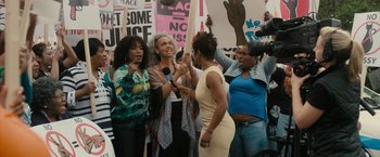 Movie still from “Chi-Raq” (2015), directed by Spike Lee – A group of people standing next to each other holding signs and microphones; Medium shot, High angle