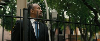 Movie still from “Chi-Raq” (2015), directed by Spike Lee – A man in a suit and tie standing next to a metal fence; Medium shot, Low angle