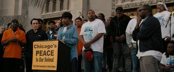 Movie still from “Chi-Raq” (2015), directed by Spike Lee – A group of people standing in front of a podium; Medium shot, High angle