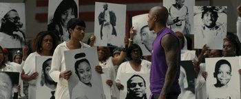 Movie still from “Chi-Raq” (2015), directed by Spike Lee – A group of people holding up pictures of people; Medium shot, High angle