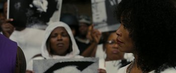 Movie still from “Chi-Raq” (2015), directed by Spike Lee – A group of people holding up signs in front of a crowd; Close Up shot, Over the shoulder angle
