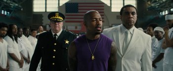 Movie still from “Chi-Raq” (2015), directed by Spike Lee – A group of men standing next to each other in front of an american flag; Medium shot, Over the shoulder angle