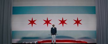 Movie still from “Chi-Raq” (2015), directed by Spike Lee – A man standing in front of a chicago flag; Wide shot, High angle