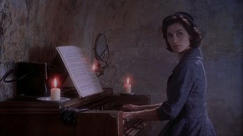 Movie still from “Chocolat” (2000), directed by Lasse Hallström – A woman is playing the organ in a room with candles; Medium shot, High angle