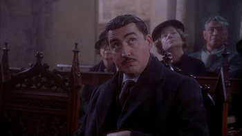 Movie still from “Chocolat” (2000), directed by Lasse Hallström – A man in a suit and tie sitting next to a woman; Close Up shot, Low angle