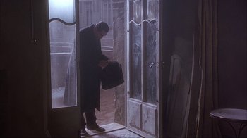 Movie still from “Chocolat” (2000), directed by Lasse Hallström – A man in a black coat is standing in front of a door; Wide shot, Low angle