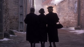 Movie still from “Chocolat” (2000), directed by Lasse Hallström – A group of three women standing next to each other on a street; Medium shot, High angle