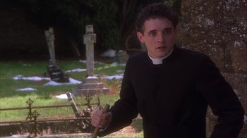 Movie still from “Chocolat” (2000), directed by Lasse Hallström – A man wearing a priest's outfit in front of an old grave; Medium shot, Low angle