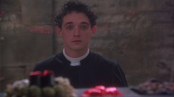 Movie still from “Chocolat” (2000), directed by Lasse Hallström – A man wearing a priest's outfit looking at the camera; Close Up shot, Over the shoulder angle