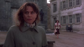 Movie still from “Chocolat” (2000), directed by Lasse Hallström – A woman standing in front of a building with another woman walking in the background; Medium shot, Over the shoulder angle