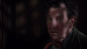 Movie still from “Chocolat” (2000), directed by Lasse Hallström – An older man with a curly hair holding a steering wheel in a dark room; Close Up shot, Over the shoulder angle