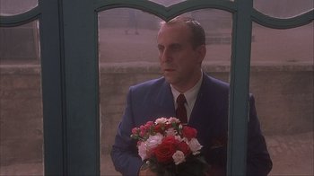 Movie still from “Chocolat” (2000), directed by Lasse Hallström – A man holding a bouquet of flowers looking out of a window; Medium shot, Low angle