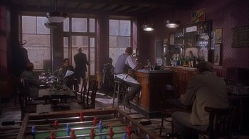 Movie still from “Chocolat” (2000), directed by Lasse Hallström – A man sitting at a bar in front of a table with foosball tables; Wide shot, High angle