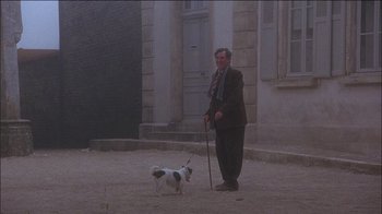 Movie still from “Chocolat” (2000), directed by Lasse Hallström – A man and a dog are standing in the dirt; Wide shot, Low angle