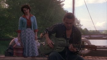 Movie still from “Chocolat” (2000), directed by Lasse Hallström – A man playing an instrument while a woman looks on; Medium shot, Over the shoulder angle