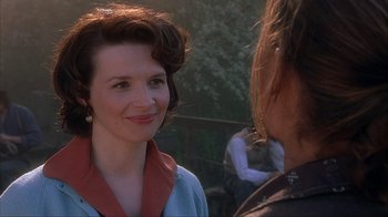 Movie still from “Chocolat” (2000), directed by Lasse Hallström – A woman smiles at the camera as a man looks on; Close Up shot, Over the shoulder angle