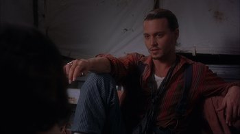Movie still from “Chocolat” (2000), directed by Lasse Hallström – A man sitting on the ground wearing a plaid shirt; Medium shot, Over the shoulder angle