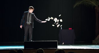 Movie still from “Chronicle” (2012), directed by Josh Trank – A man on a stage throwing papers into the air; Wide shot, Over the shoulder angle