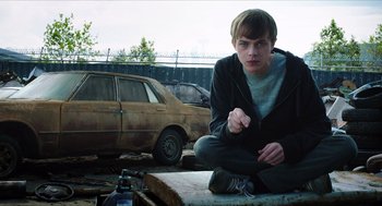 Movie still from “Chronicle” (2012), directed by Josh Trank – A young man sitting on the side of the road near an old car; Medium shot, Over the shoulder angle