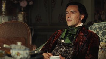 Movie still from “Cinderella” (2015), directed by Kenneth Branagh – A man sitting at a table holding a cup of coffee; Medium shot, Low angle