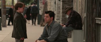 Movie still from “Cinderella Man” (2005), directed by Ron Howard – A man sitting on the ground on the sidewalk; Medium shot, Over the shoulder angle