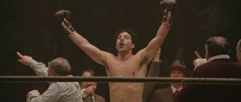 Movie still from “Cinderella Man” (2005), directed by Ron Howard – A shirtless man in a boxing ring raising his hands; Medium shot, Low angle