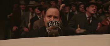 Movie still from “Cinderella Man” (2005), directed by Ron Howard – A man with his mouth over his face is sitting in front of a microphone; Medium shot, Low angle