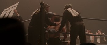 Movie still from “Cinderella Man” (2005), directed by Ron Howard – A group of men standing around a man in a boxing ring; Wide shot, Over the shoulder angle